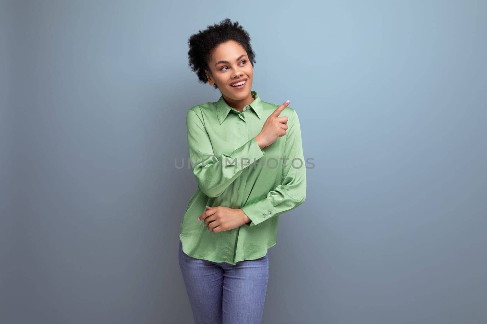 cute young brunette hispanic woman dressed in a green blouse points with her hand on the background with copy space. people lifestyle concept.