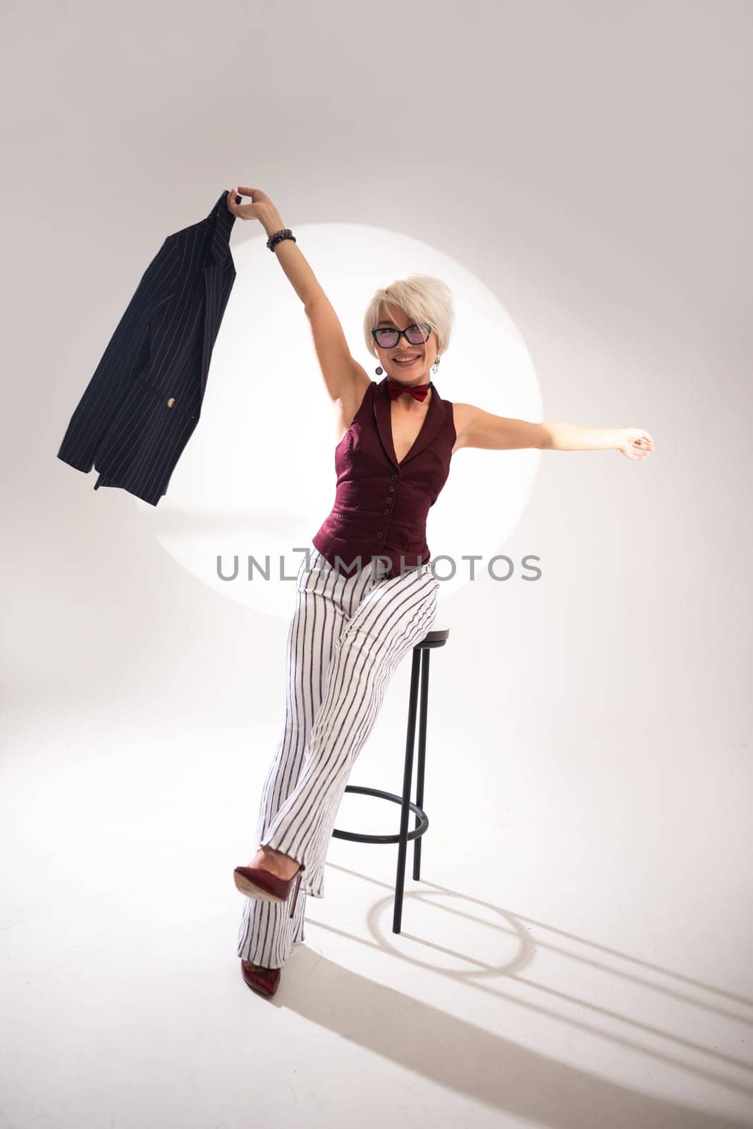 studio photo of a sexy girl in glasses and a suit on a bar stool on a light background