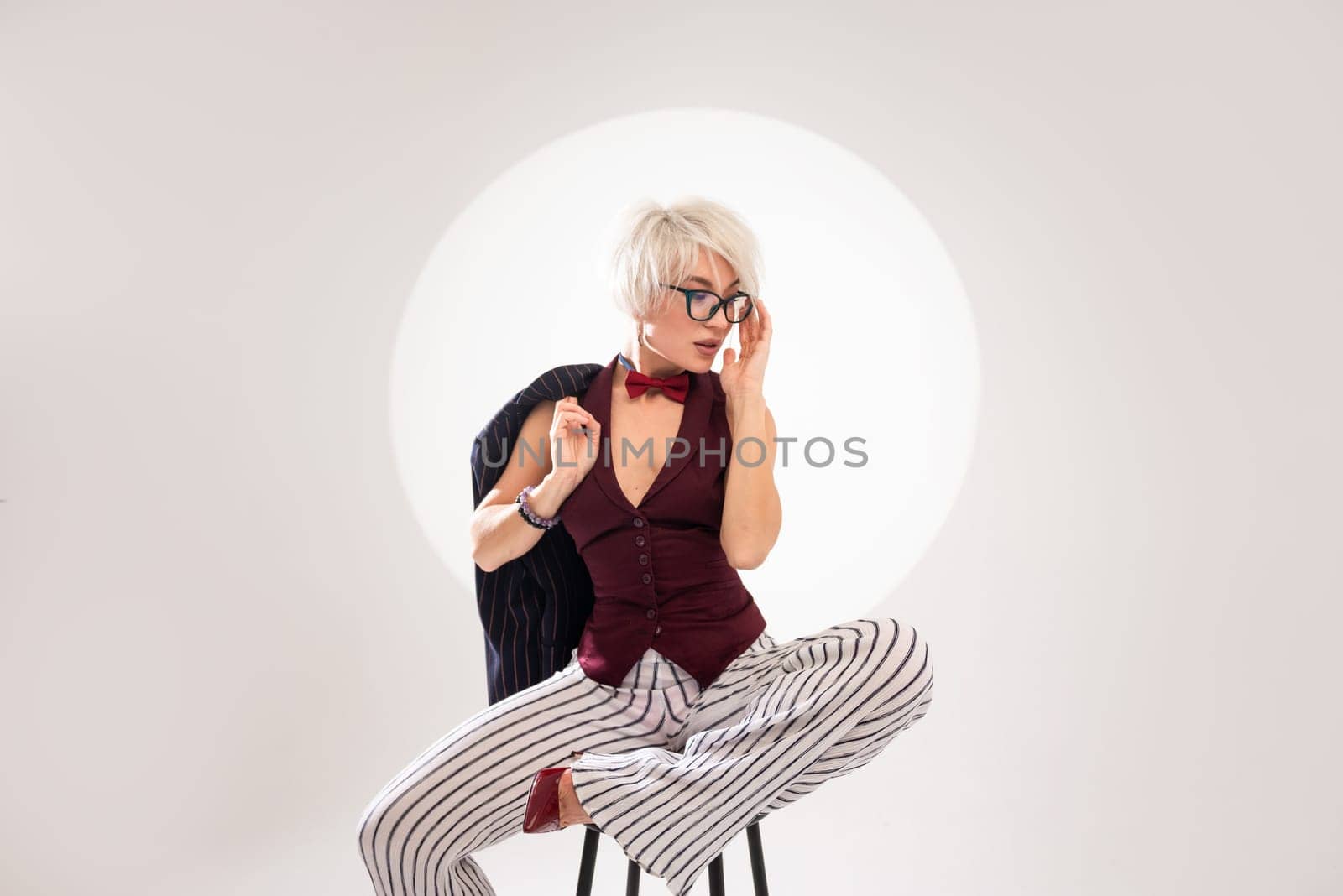studio photo of a sexy girl in glasses and a suit on a bar stool on light background by Rotozey
