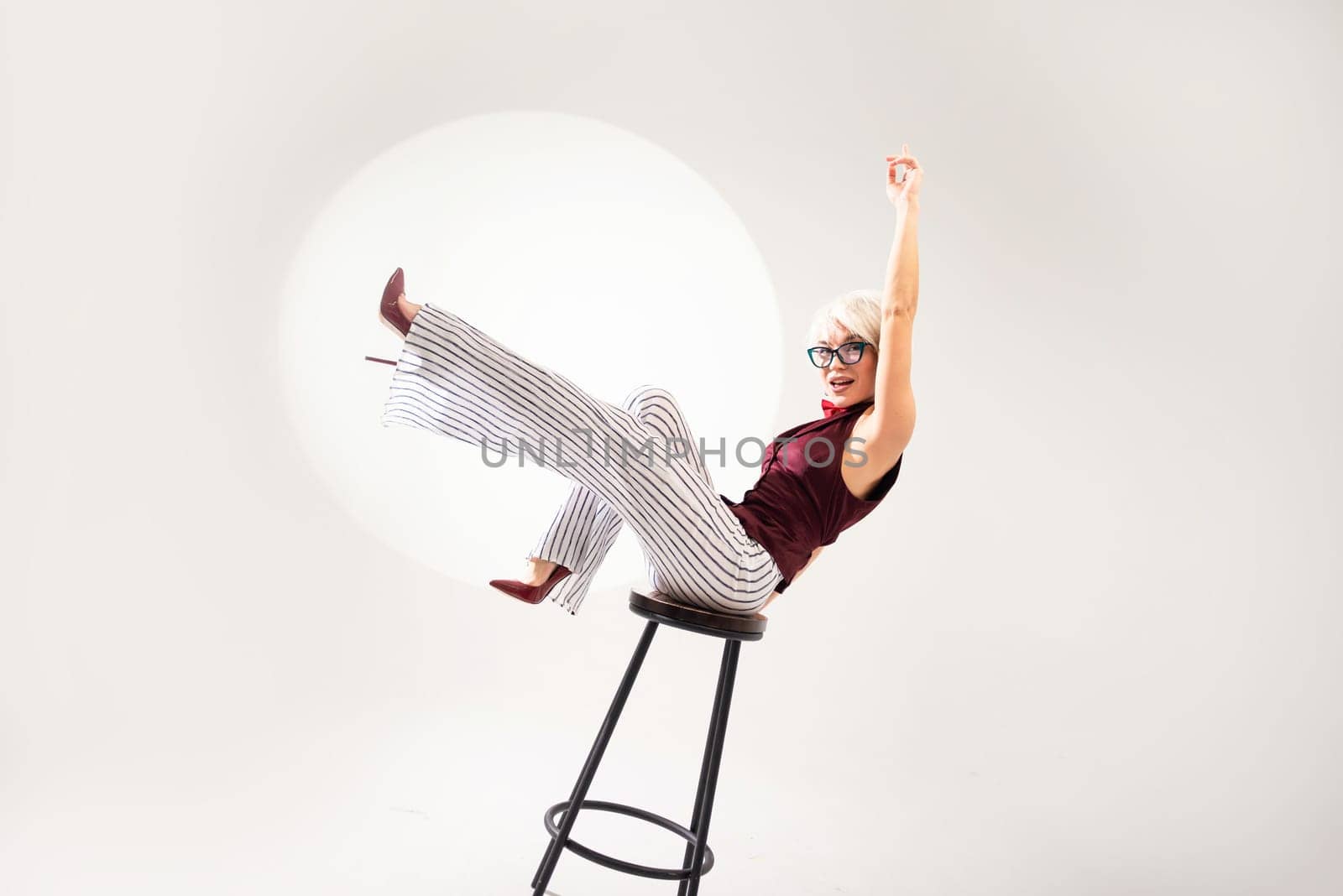 studio photo of a sexy girl in glasses and a suit on a bar stool on a light background