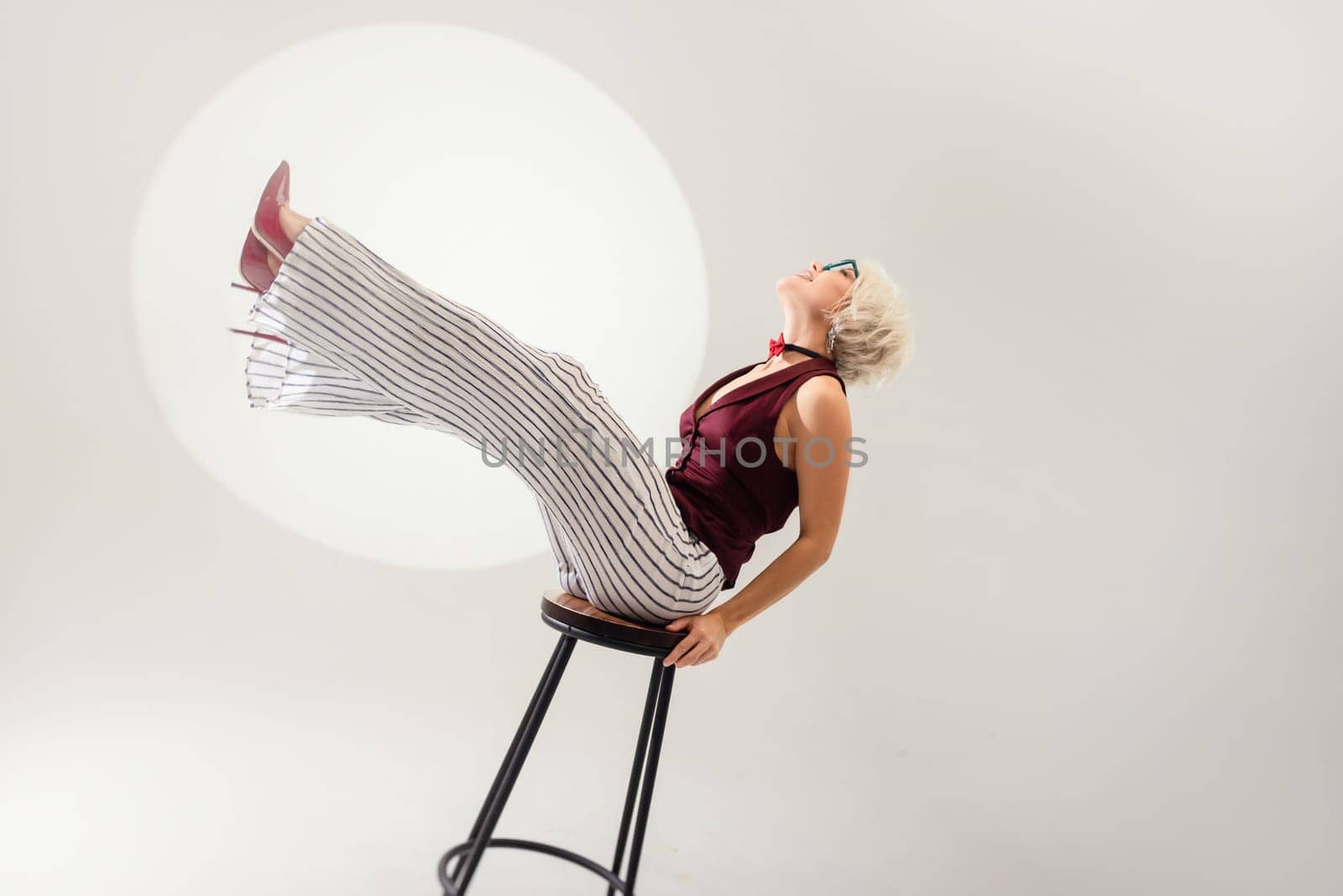 studio photo of a sexy girl in glasses and a suit on a bar stool on a light background