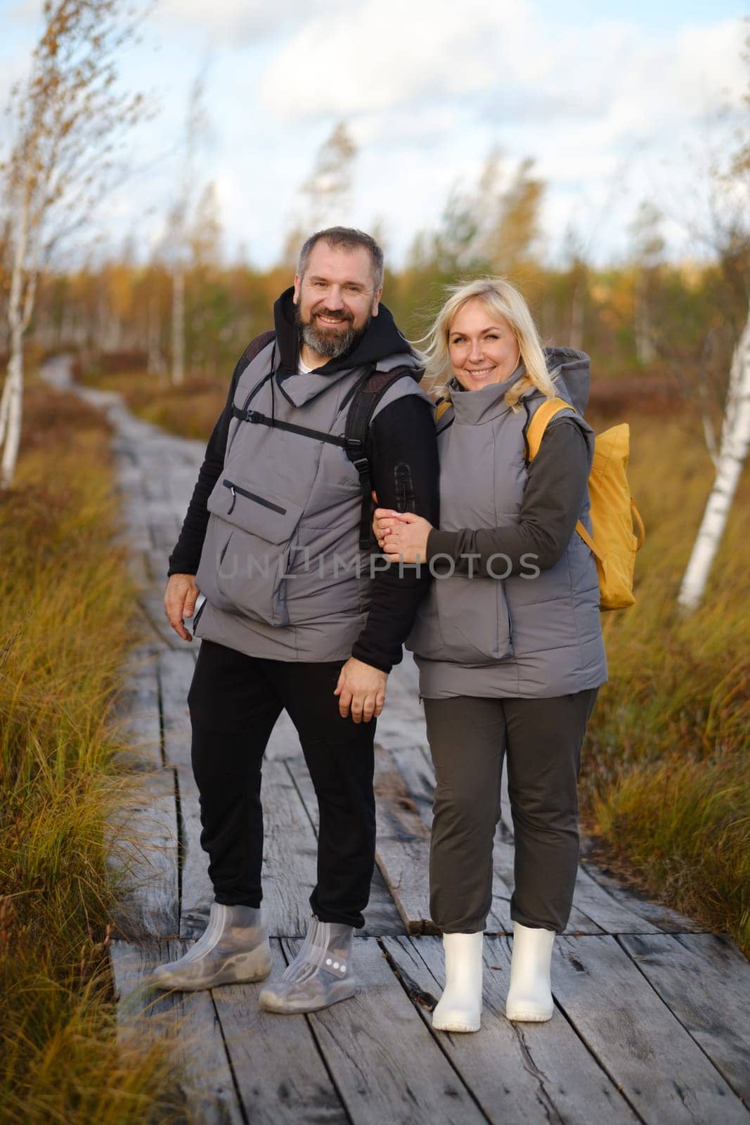 People in boots stand hugging on a wooden path in a swamp in Yelnya, Belarus.