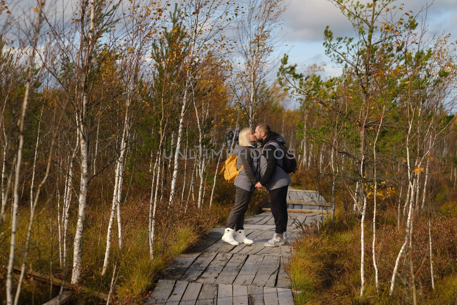 Tourists with backpacks kiss a wooden path in a swamp in Yelnya, Belarus.