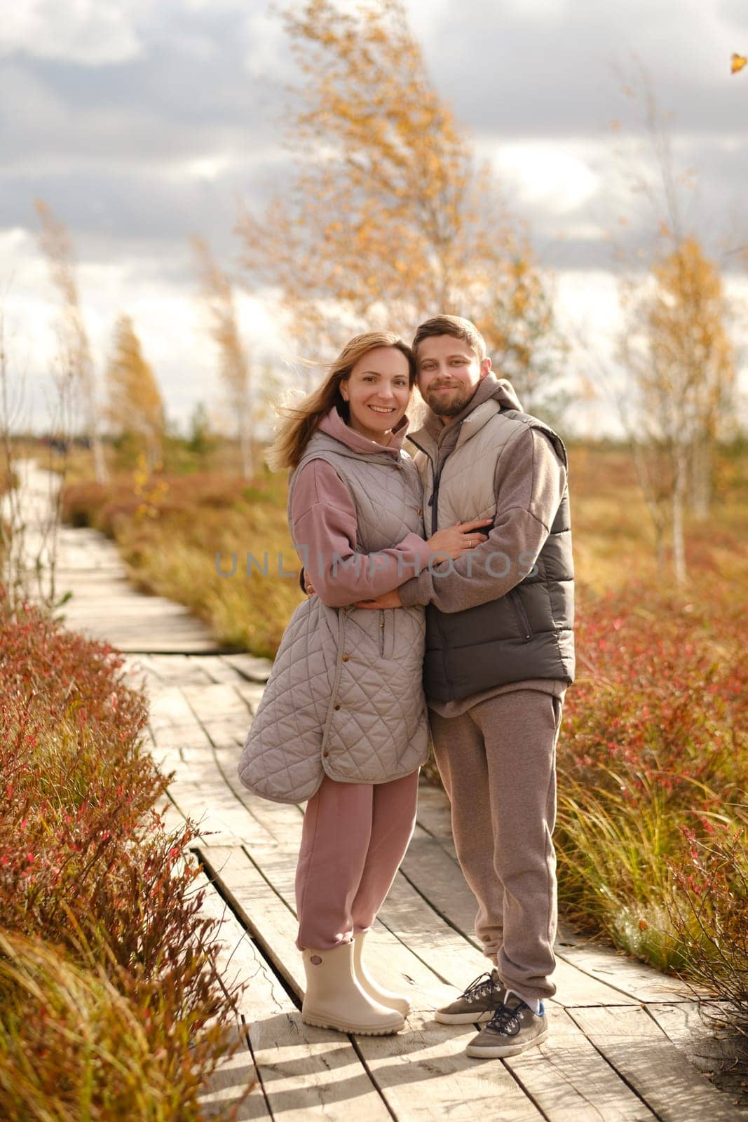 People in boots stand hugging on a wooden path in a swamp in Yelnya, Belarus by Lobachad