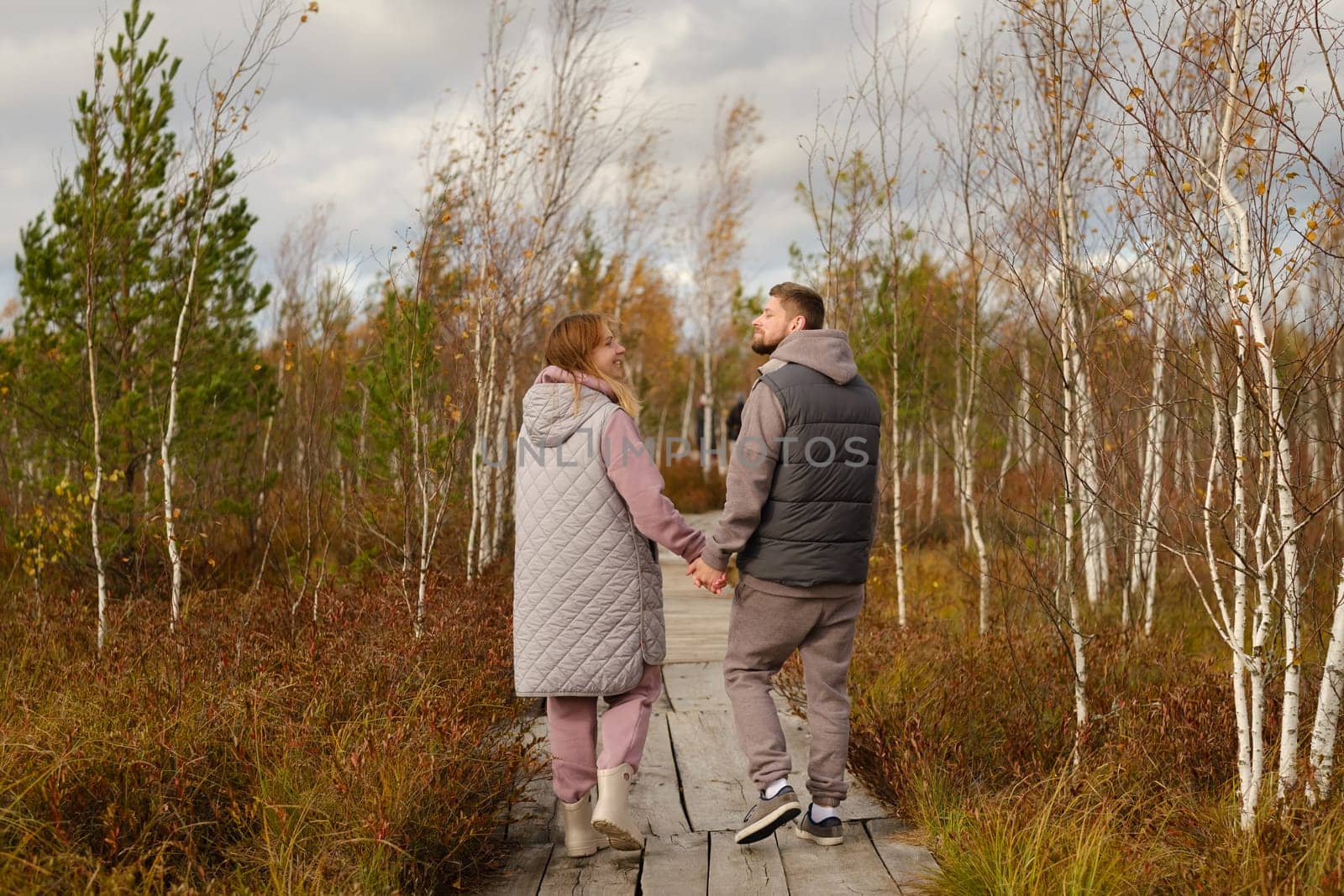 Two tourists walk along a wooden path in a swamp in Yelnya, Belarus by Lobachad