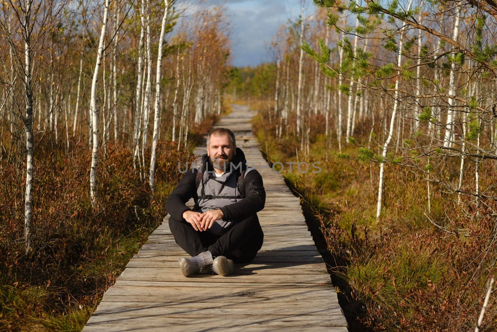 A man sits on a wooden path in a swamp in Yelnya, Belarus by Lobachad