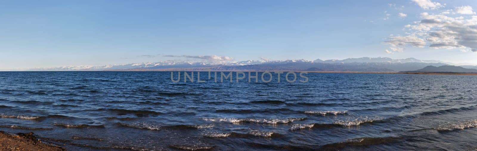 Blue calm water in Issyk-Kul lake with mountains on background at summer day - wide panorama by z1b