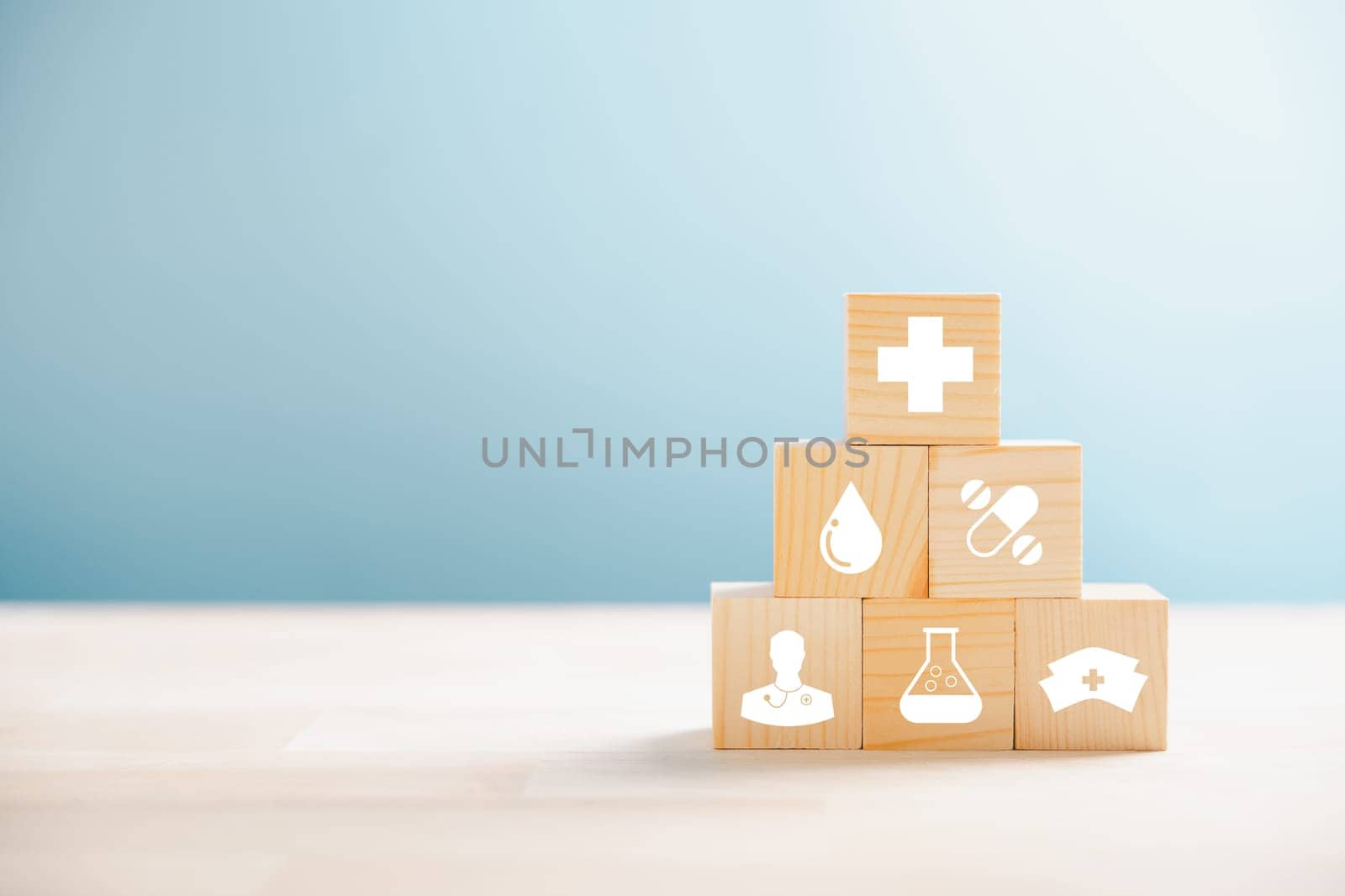 Wooden cubes crafted into a pyramid, embodying the healthcare and insurance concept. Medical insurance icon atop reflects protection. Blue background with space for promoting Health Insurance ideas.