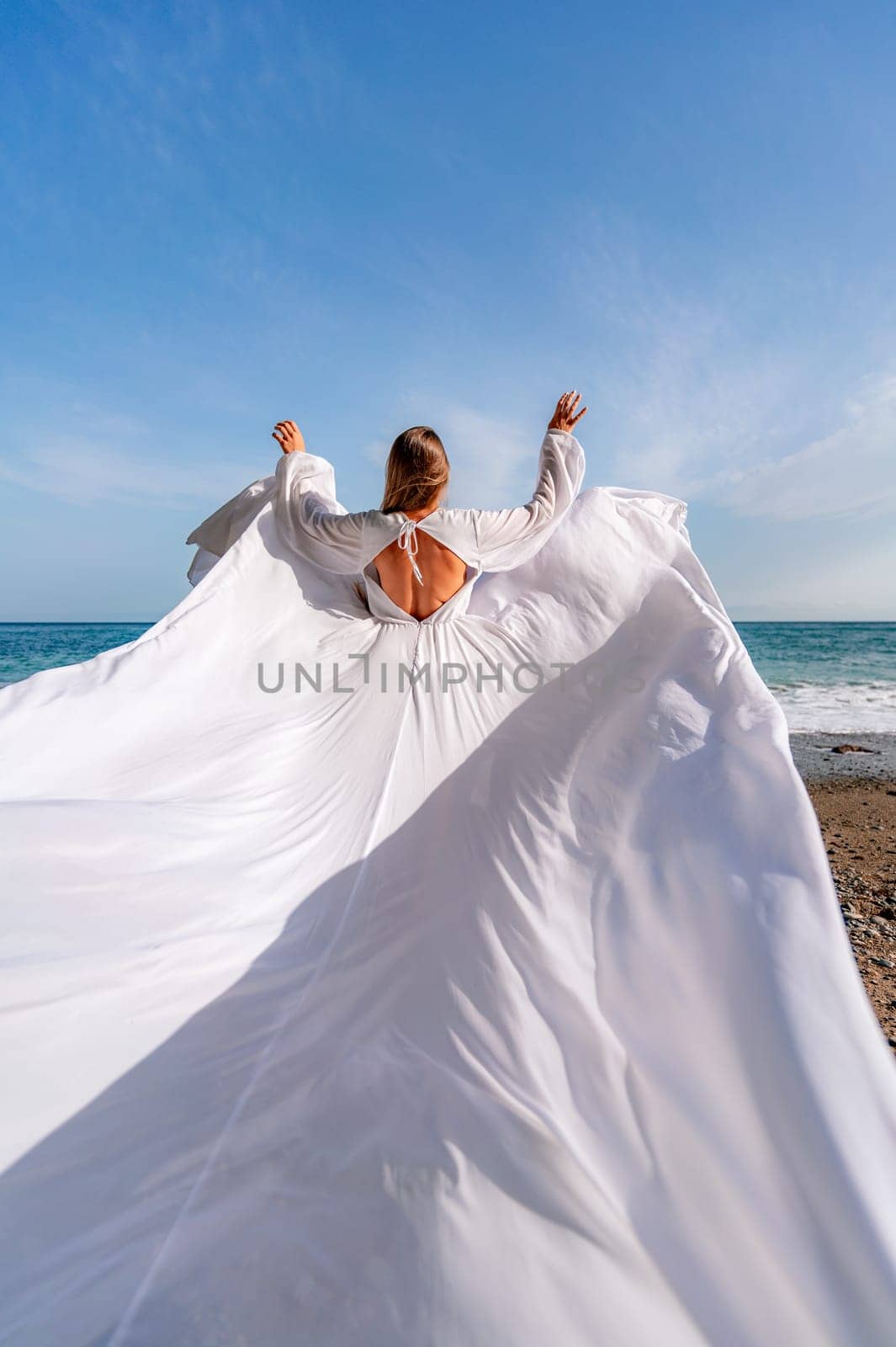 Woman beach white dress flying on Wind. Summer Vacation. A happy woman takes vacation photos to send to friends. by Matiunina