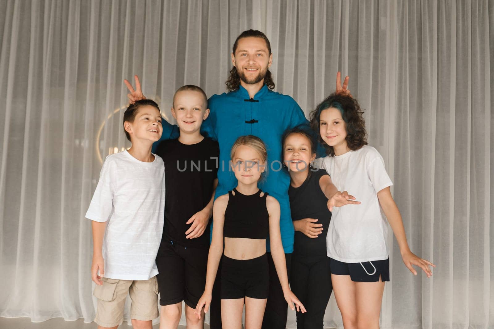 A joint portrait of a yoga coach and children standing in a fitness room.