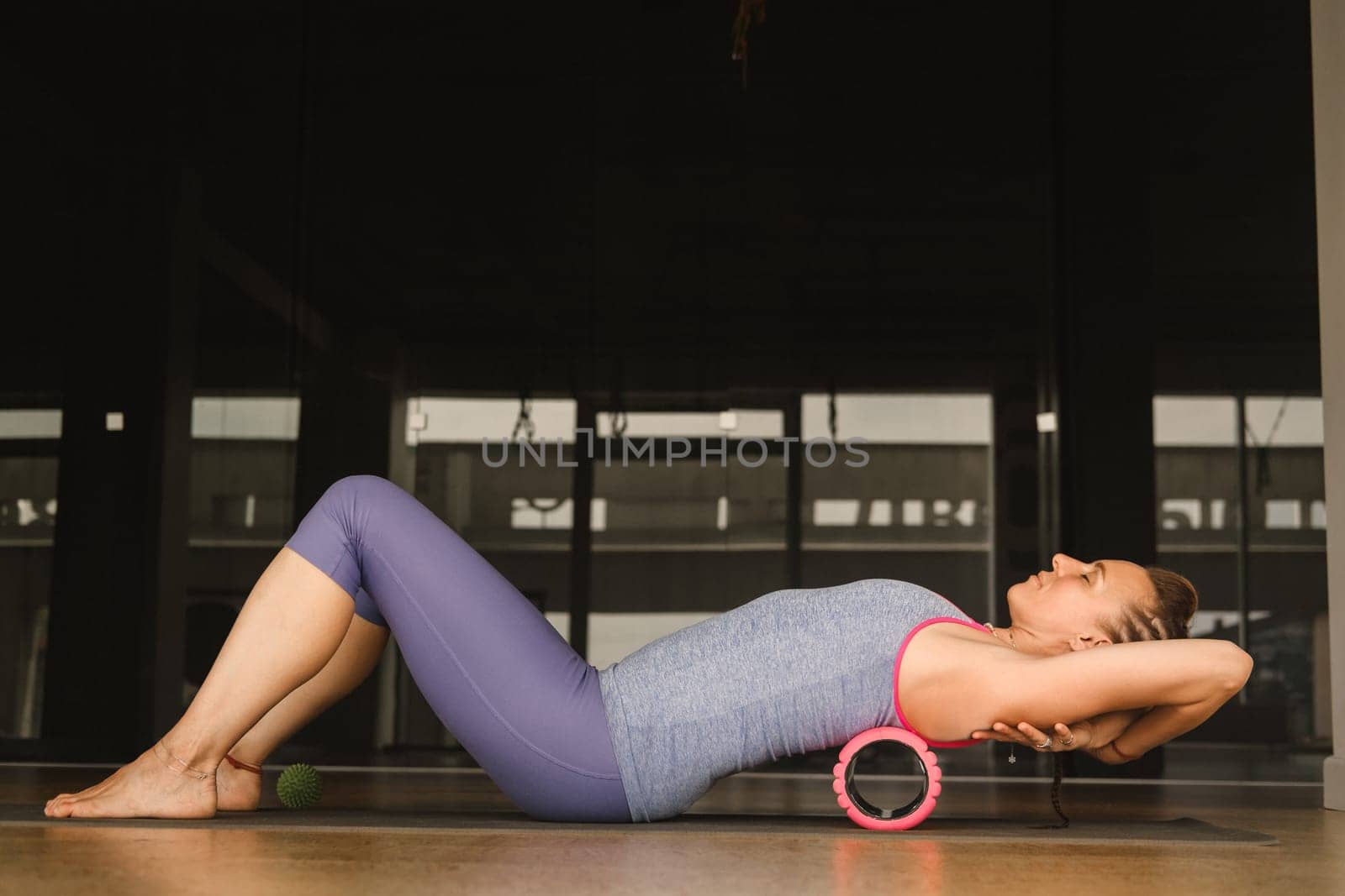 Slender girl doing yoga with a big massage roller on the floor.