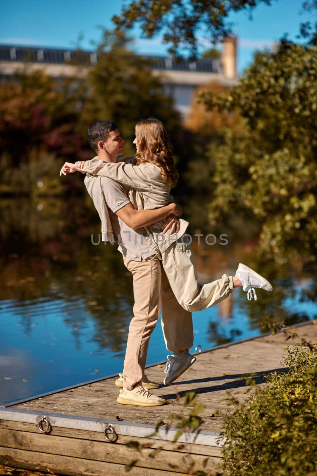 A happy couple in love in casual clothes travel together, hike and have fun in the fall forest on a weekend in nature in autumn outdoors, selective focus. Handsome man embracing with passion his girlfriend outdoor under the leaves of trees on the embankment. Love history. Happy people concept