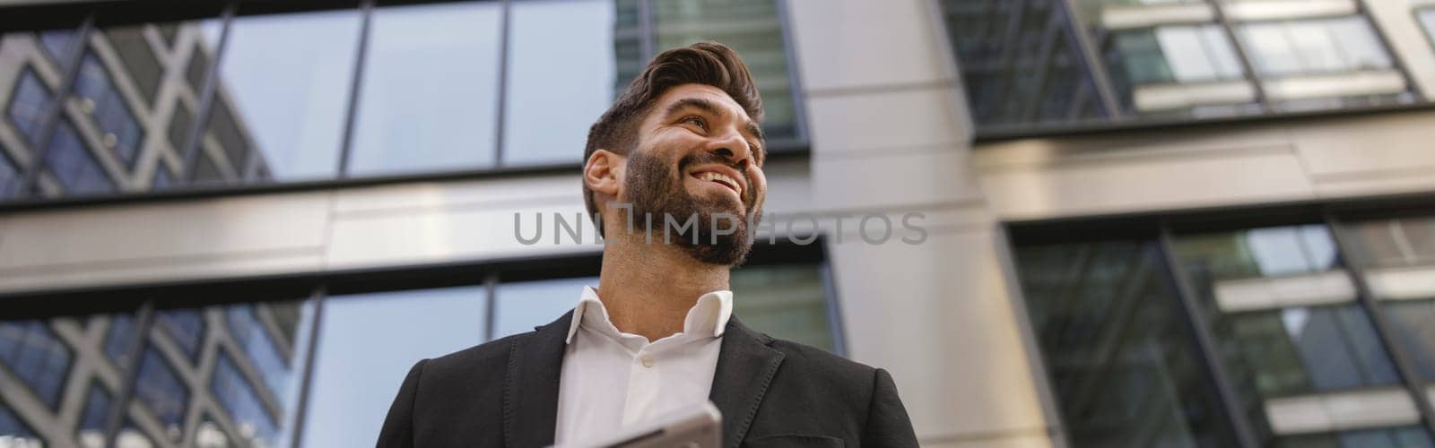 Stylish male manager with laptop standig on office terrace and looks away. High quality photo