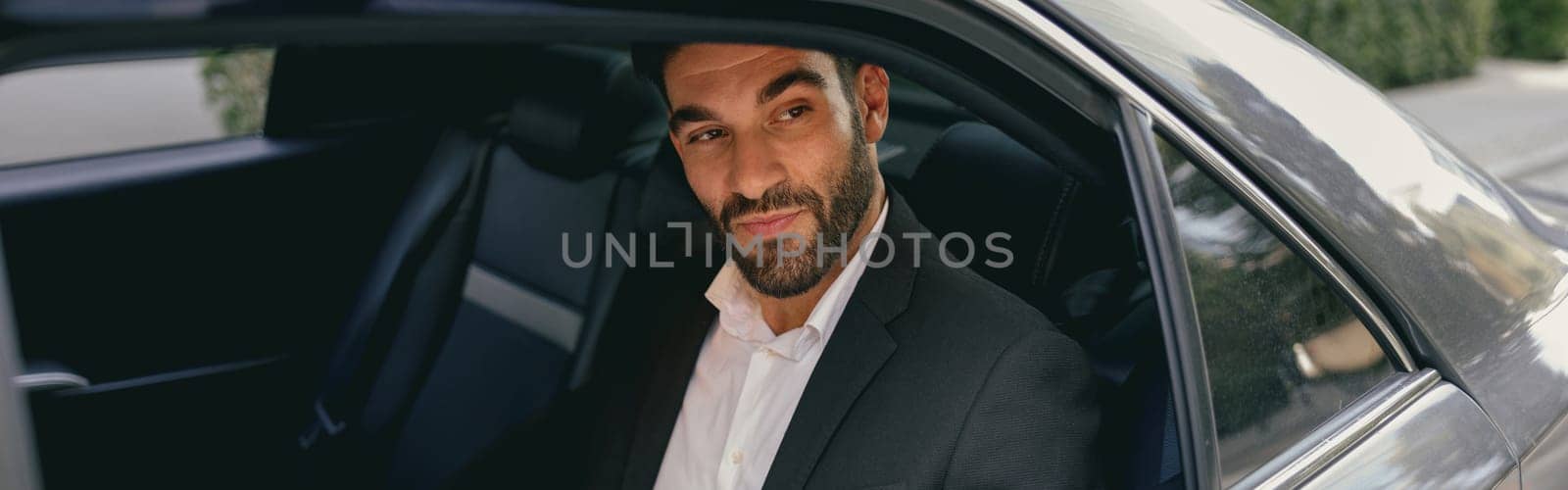 Confidence businessman sitting on car backseat and working with documents and use laptop by Yaroslav_astakhov