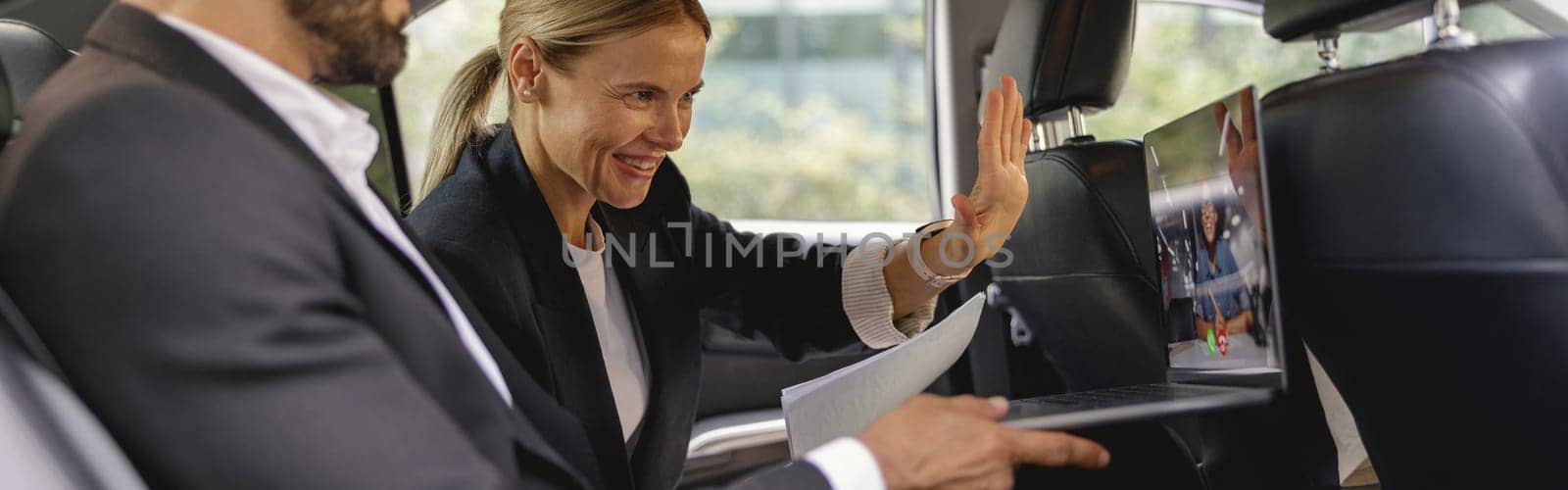 Smiling business colleagues have online meeting using laptop while sitting in car back seats