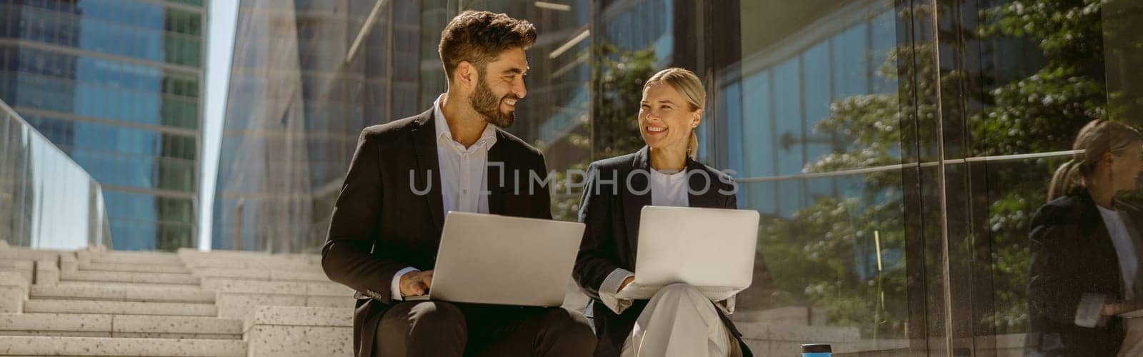 Smiling businessman and businesswomen working outdoor on laptop with new startup project