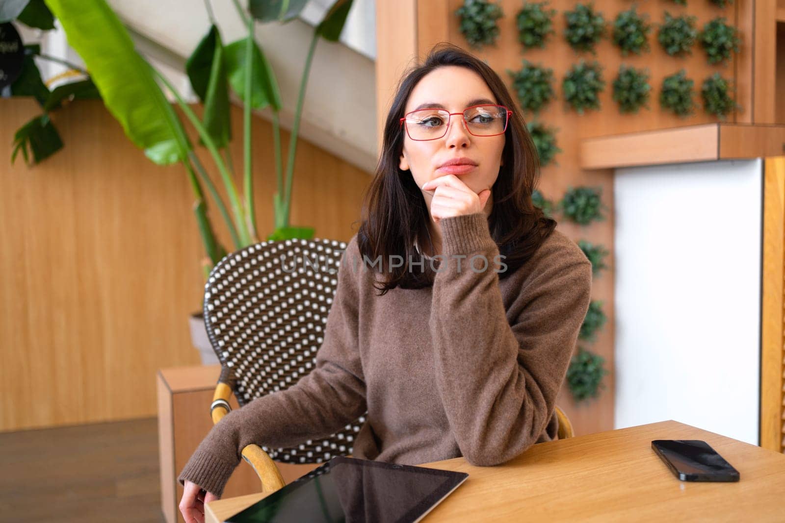 Business woman wear glasses sitting at desk thinking and looking away. Woman employee relaxes in break room and plans out rest of day. Female dressed in smart casual and glasses sits in break room