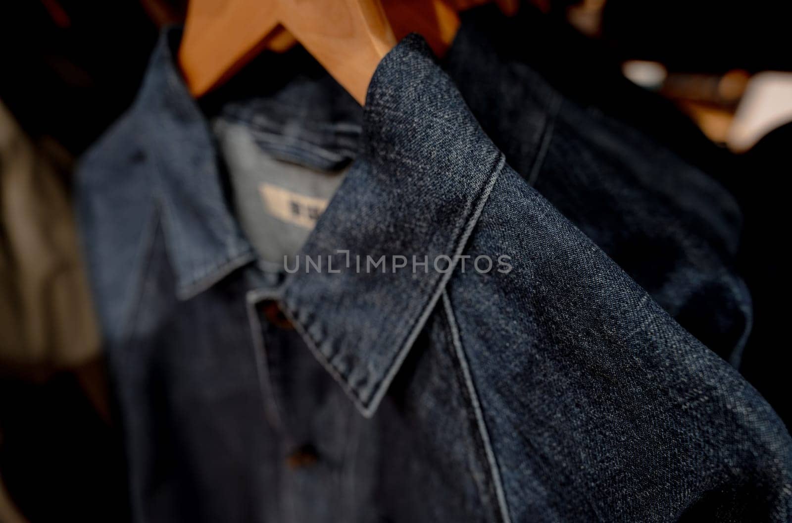 Selective focus on jacket jeans hanging on rack in clothes shop. Denim jeans with jeans pattern. Textile industry. Jeans fashion and shopping concept. Clothing concept. Denim jacket on rack for sale. by Fahroni