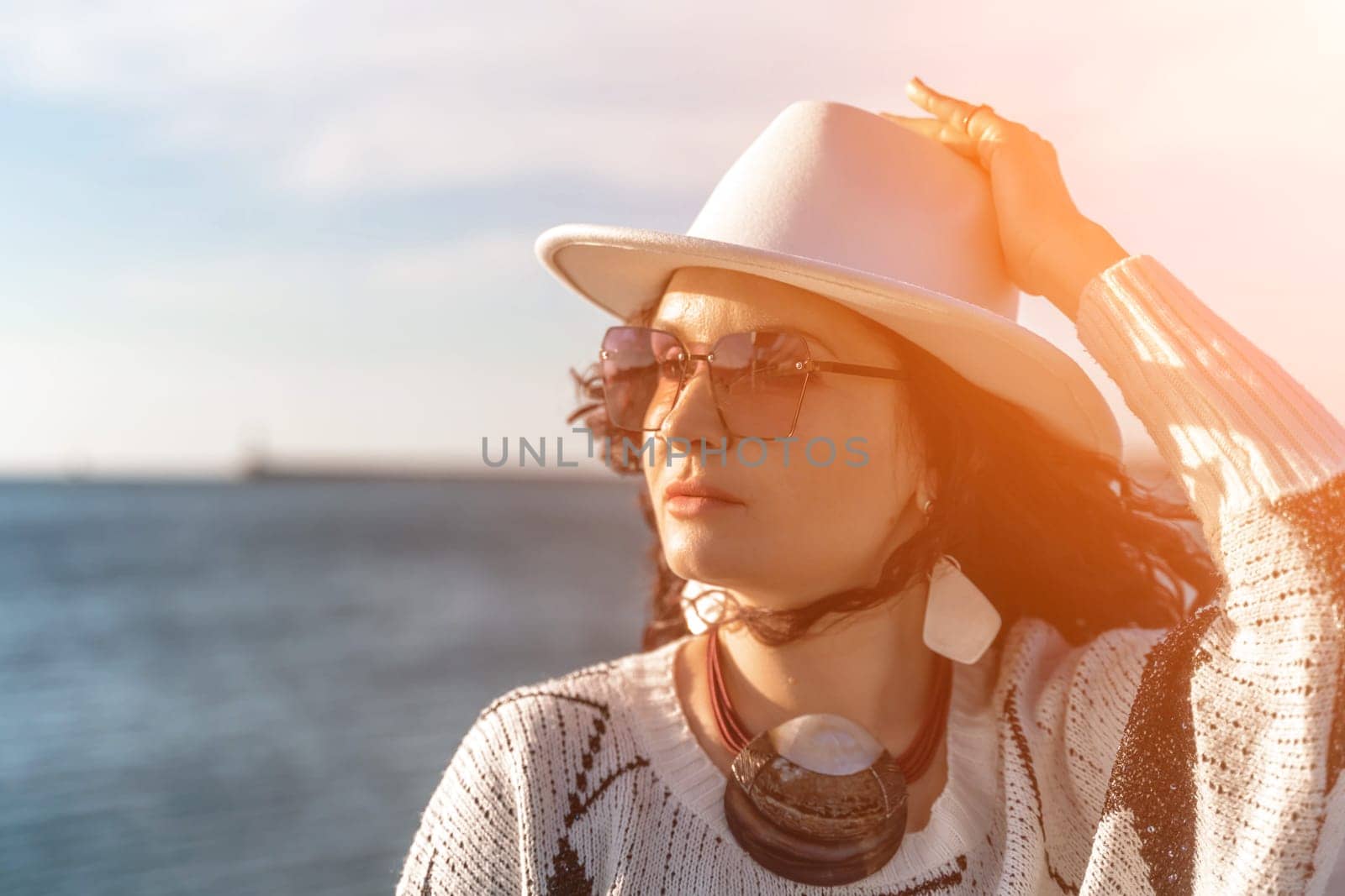 Portrait of a curly haired woman in a white hat and glasses on the background of the sea