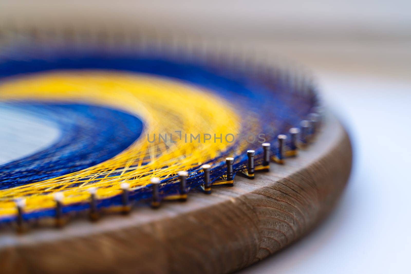 Colored thread mandala on a wooden board with nails. Mandala Moon Harmony Sun esotericism and psychology pictures from yellow and blue silk threads