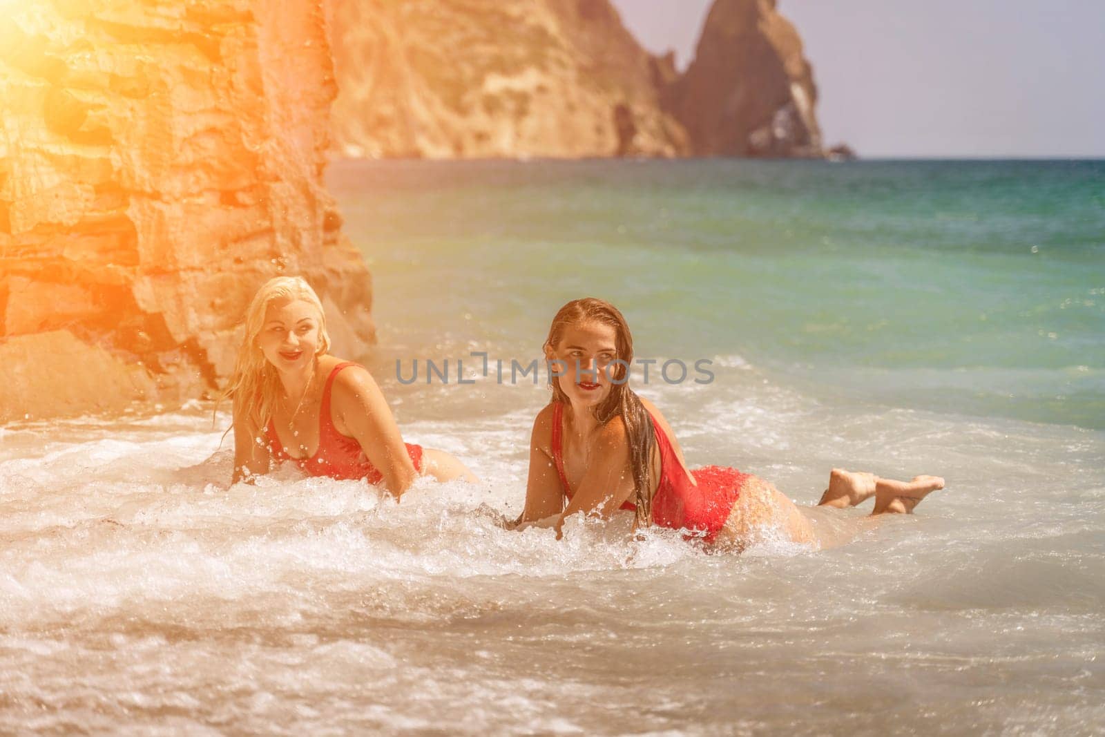 Women ocean play. Seaside, beach daytime, enjoying beach fun. Two women in red swimsuits enjoying themselves in the ocean waves. by Matiunina