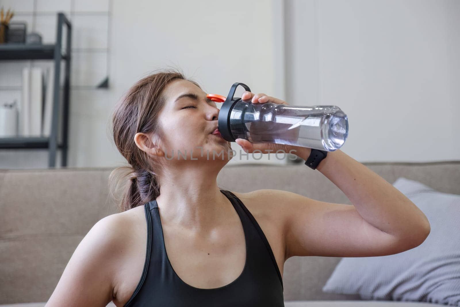 Young healthy Asian woman holds a water bottle for practicing yoga online or exercising at home..