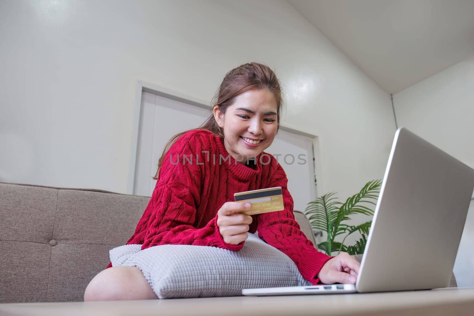online shopping. Woman buying laptop using credit card sitting on sofa at home by wichayada