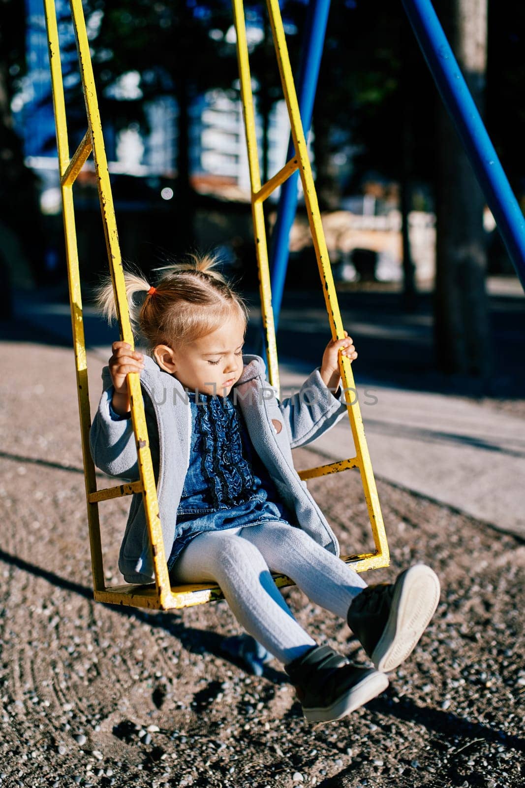 Little girl swinging on a swing holding on to the handrails. High quality photo