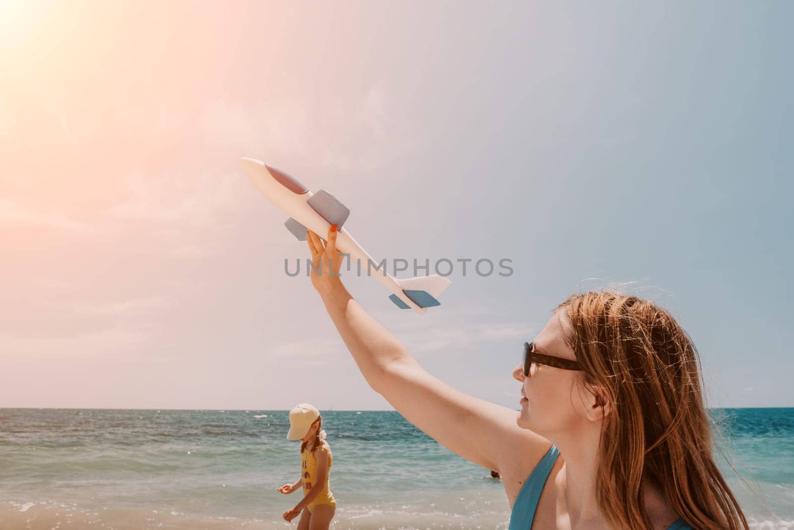 Woman hand holding toy airplane on blue sky and white clouds at seaside, dream of travel by plane. Happy woman has fun in summer vacation by sea and mountains. Lifestyle moment
