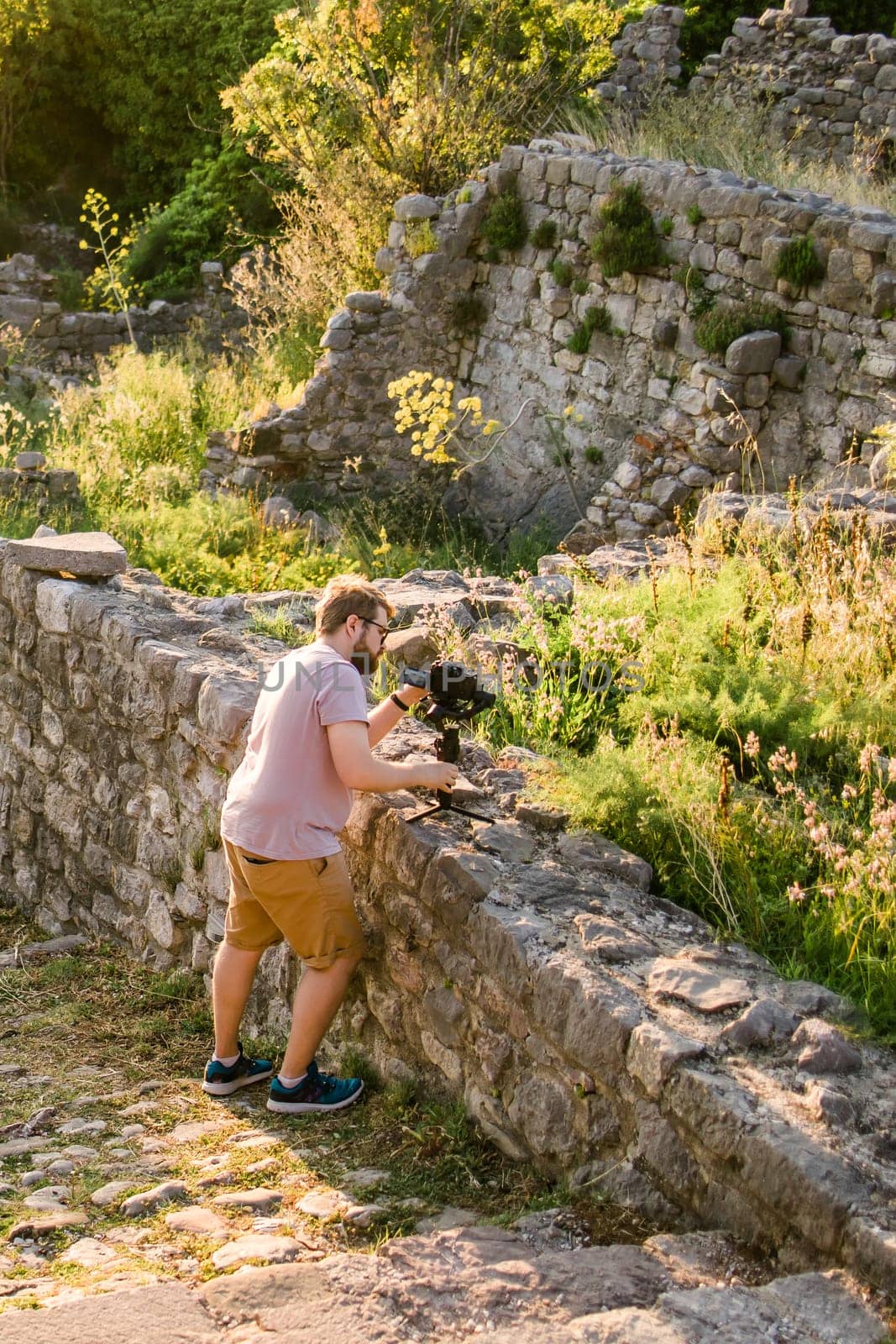 Cameraman in summer outfit with gimbal and cinema camera in his hands making travel video with old Europe Balkan nature and town on the background by Satura86