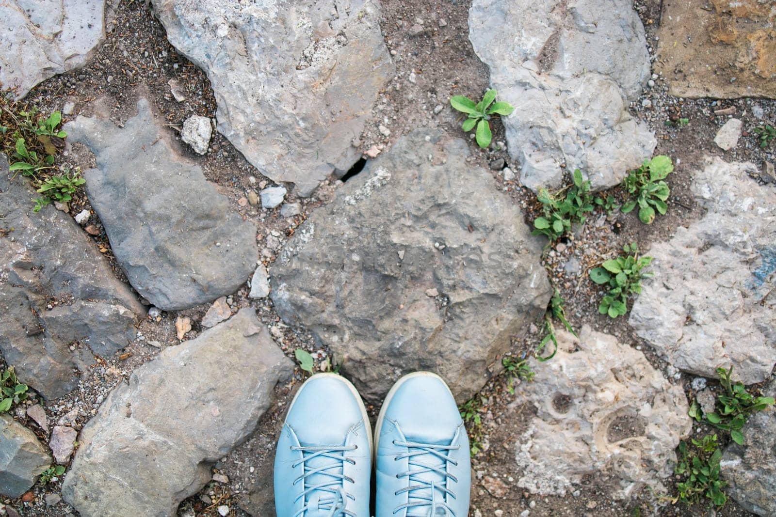 Women's legs in blue shoes on the stone pavement, top view. Photo pov. Copy space and empty place for text.