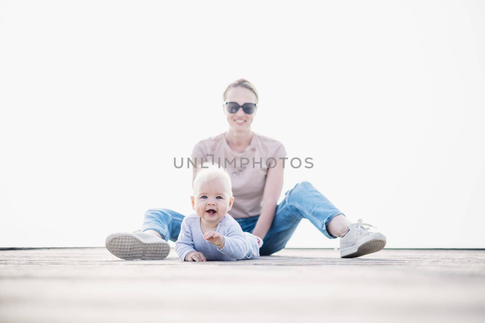 Happy family. Young mother playing with her baby boy infant oudoors on sunny autumn day. Portrait of mom and little son on wooden platform by lake. Positive human emotions, feelings, joy