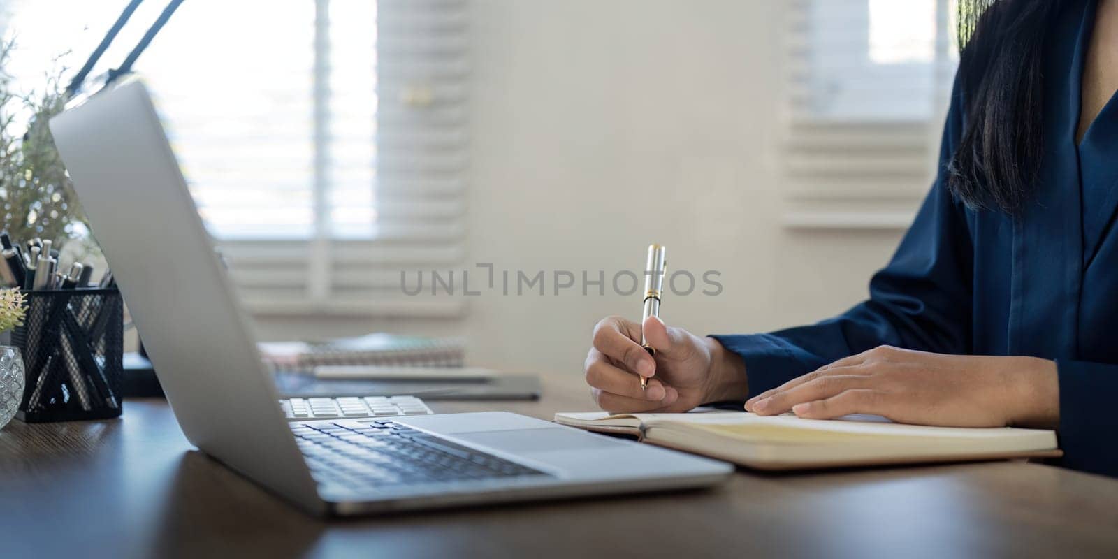 Entrepreneur working online with a laptop and taking notes in a notebook in home.