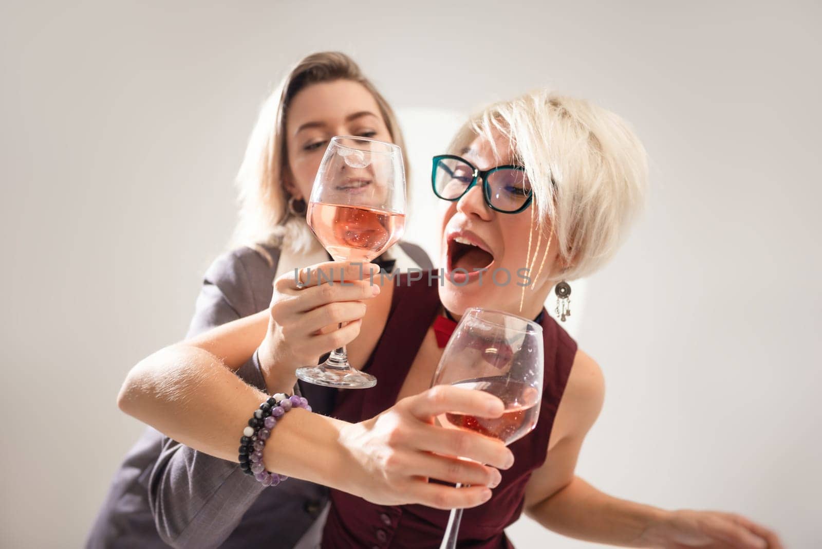 two close girlfriends with glasses of alcohol having fun laughing at a party in the studio on a white background copy paste by Rotozey