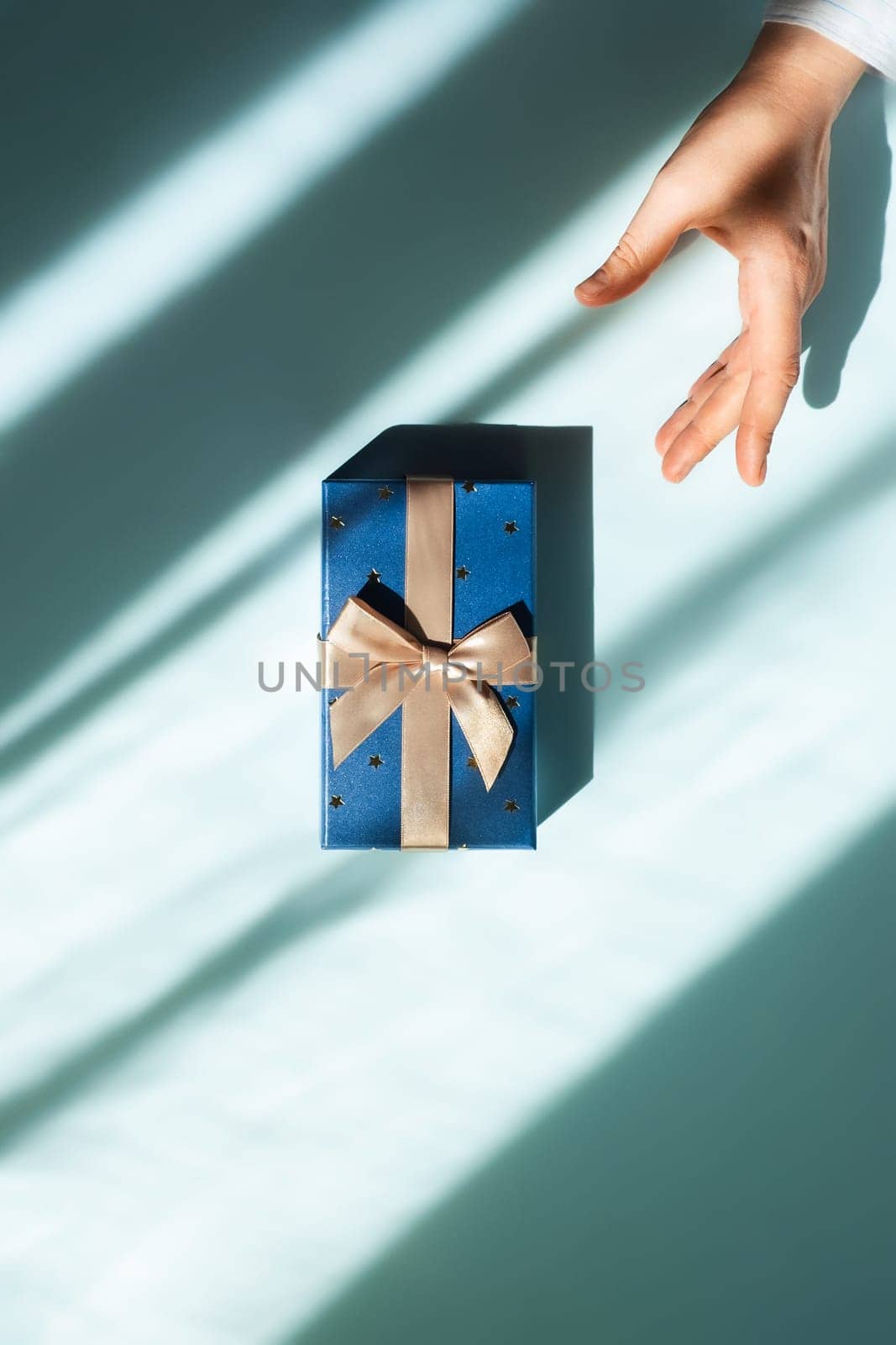 A gift in the center of the table and a woman's hand reaching for it. Flat lay picture.