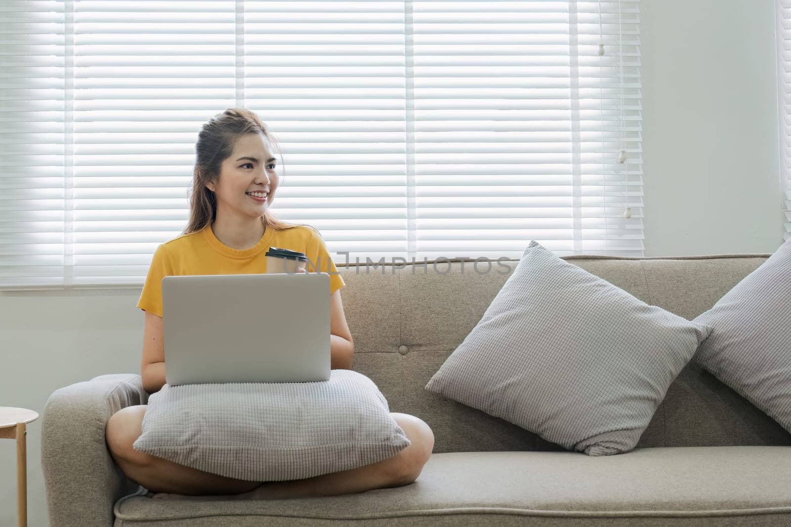 Beautiful Asian woman wearing casual clothes On the sofa using a laptop computer, entertaining with social media, relaxing, smiling and laughing. by wichayada
