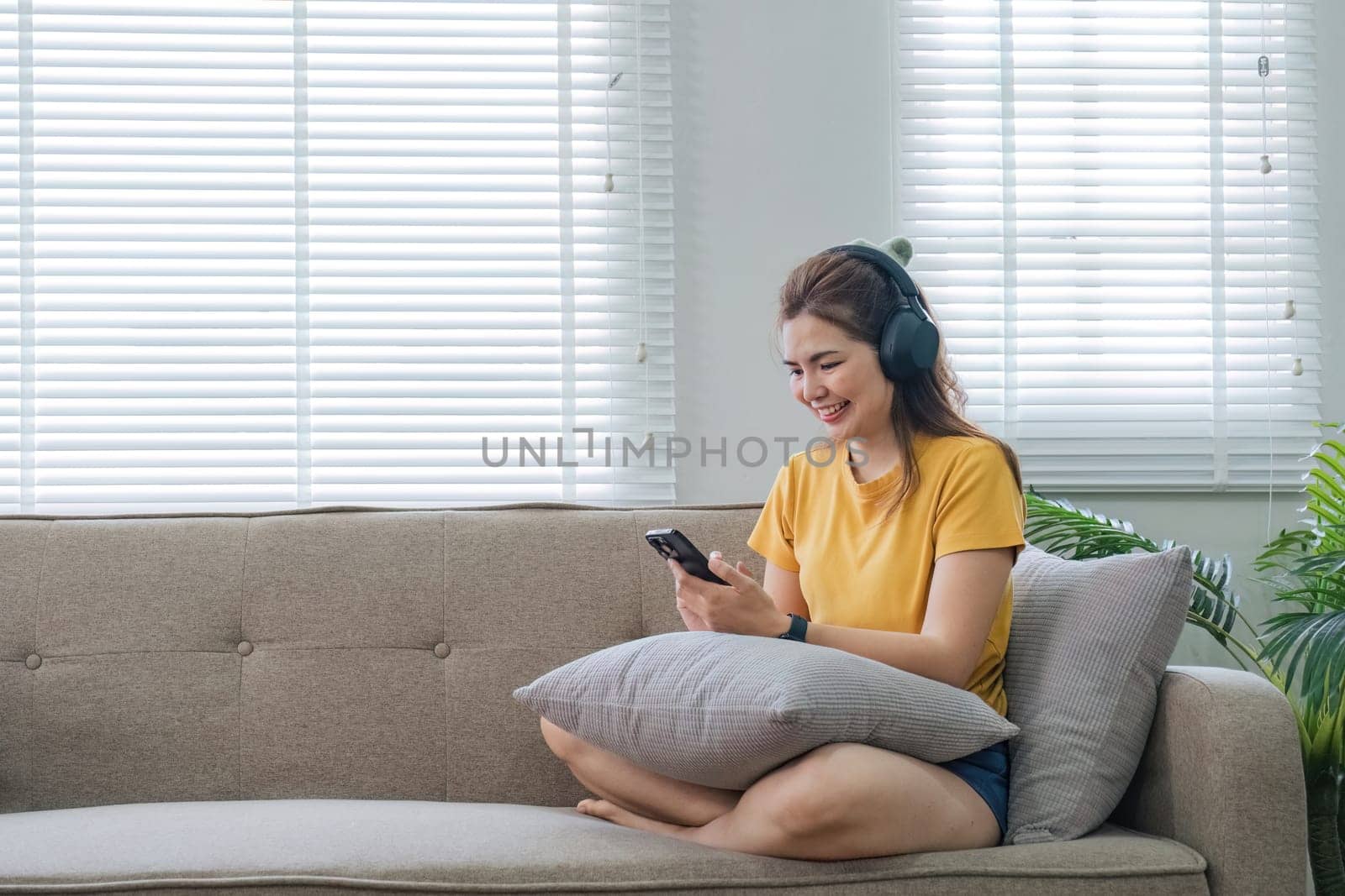 Happy asian woman listening to music from mobile phone while sitting on the the sofa at homes, Smiling girl relaxing with headphones in morning, Time to relax..
