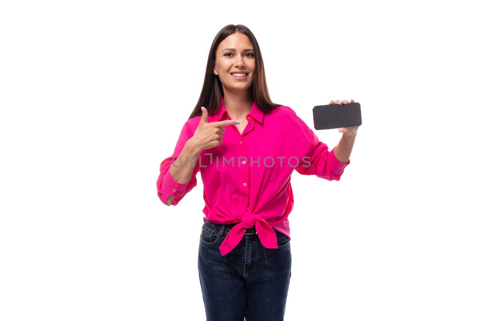 charming young brunette businesswoman dressed in a pink shirt shows the screen of a smartphone with a mockup by TRMK