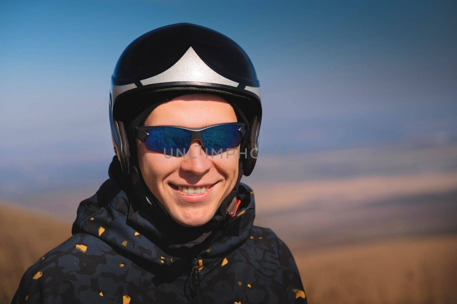 Portrait of a smiling young man with a parachute in a field. A guy paraglider in sportswear and a helmet is preparing for a flight or after landing outdoors by yanik88
