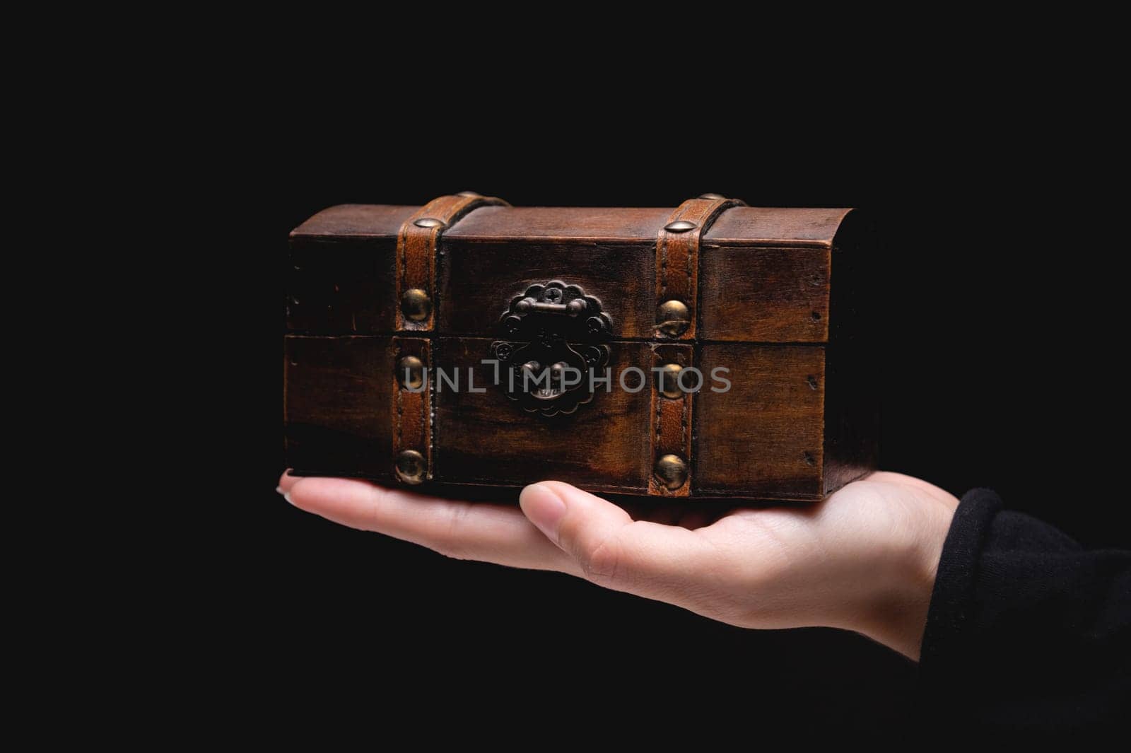 The hand of a young Caucasian woman holds a small wooden chest on a black background. Low key by yanik88