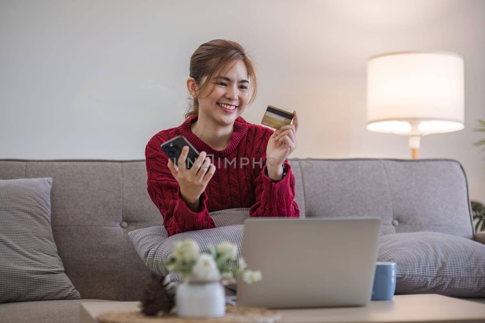 Woman holding credit card and using smartphone at home, online shopping, online banking, payment, spending money, e-commerce at store, credit card concept by wichayada