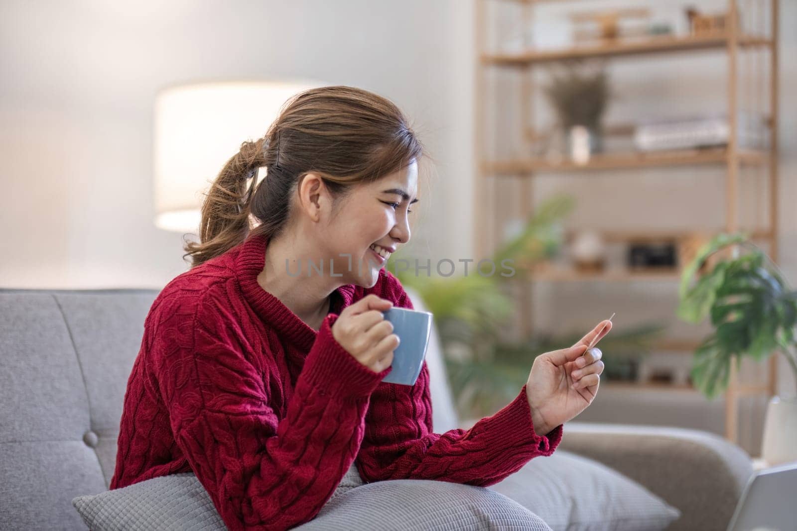 online shopping. Woman buying laptop using credit card sitting on sofa at home by wichayada