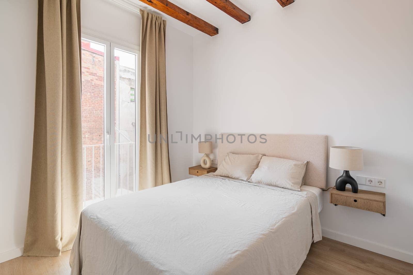 Large double bed with light linens. Spacious light bedroom with a large window to the floor. Concept of big apartment in a new building after renovation. Copyspace.