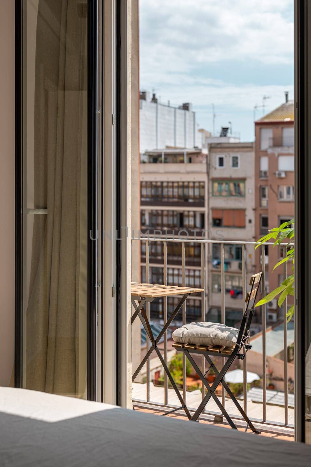 Open terrace with a table, chair and palm tree on a sunny warm summer day on the backdrop of a blurred modern houses. The concept of modern design in new buildings of a large metropoli by apavlin
