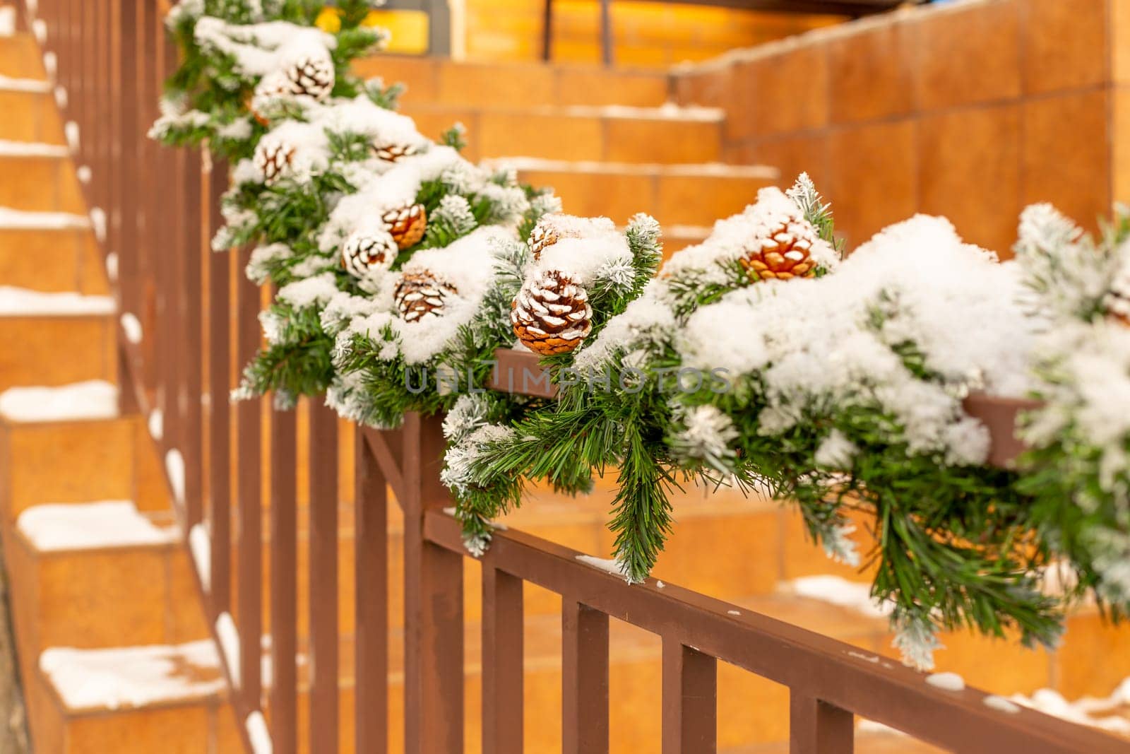 Christmas street decor under the snow. railing of the stairs are decorated with fir branches and decorative cones.Staircase decoration for the New Year. Selective focus by YuliaYaspe1979