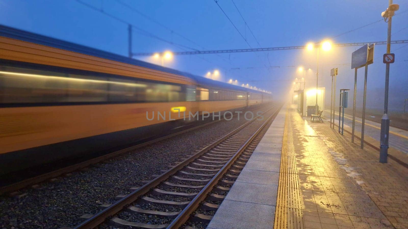 A passenger train entering the station in the fog. Night train passing the station. The concept of rail passenger transport. Night passenger train in fog by roman_nerud