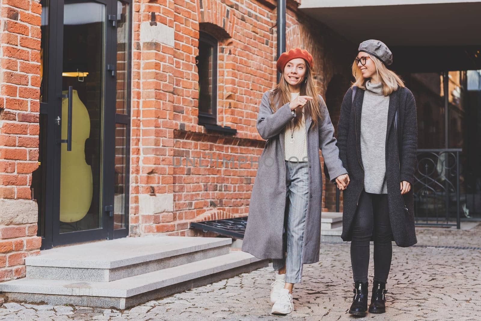 Funny female friends laughing in autumn day. Lovely girls in black coat and girl in gray coat having fun on city background. Friendship and female love