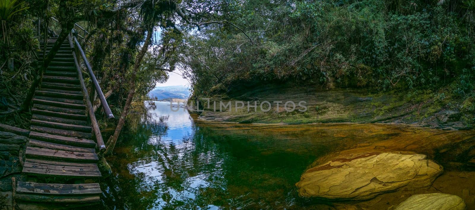 Serene cove with crystal water, surrounded by lush foliage and a wooden staircase.