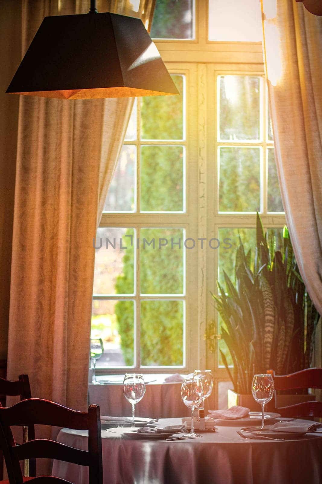 Dining table set with wine glasses by the window in a luxury restaurant interior by hotel.
