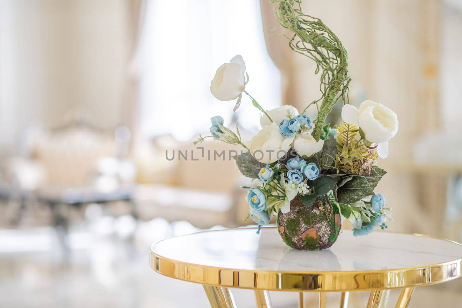 Floristry in a luxurious light gold interior. Table decorated with a vase with a bouquet of flowers, copy space.
